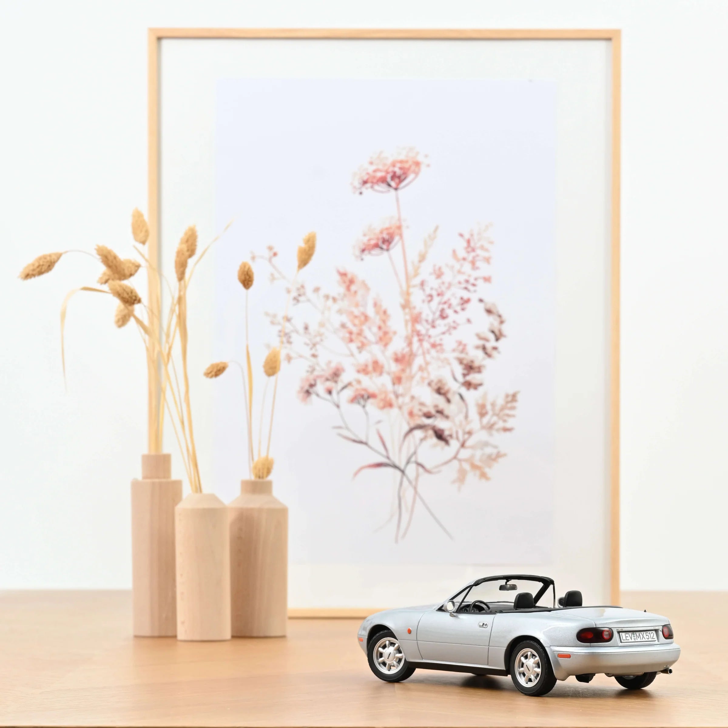 Model car on a wooden surface with decorative vases and flowers in the background