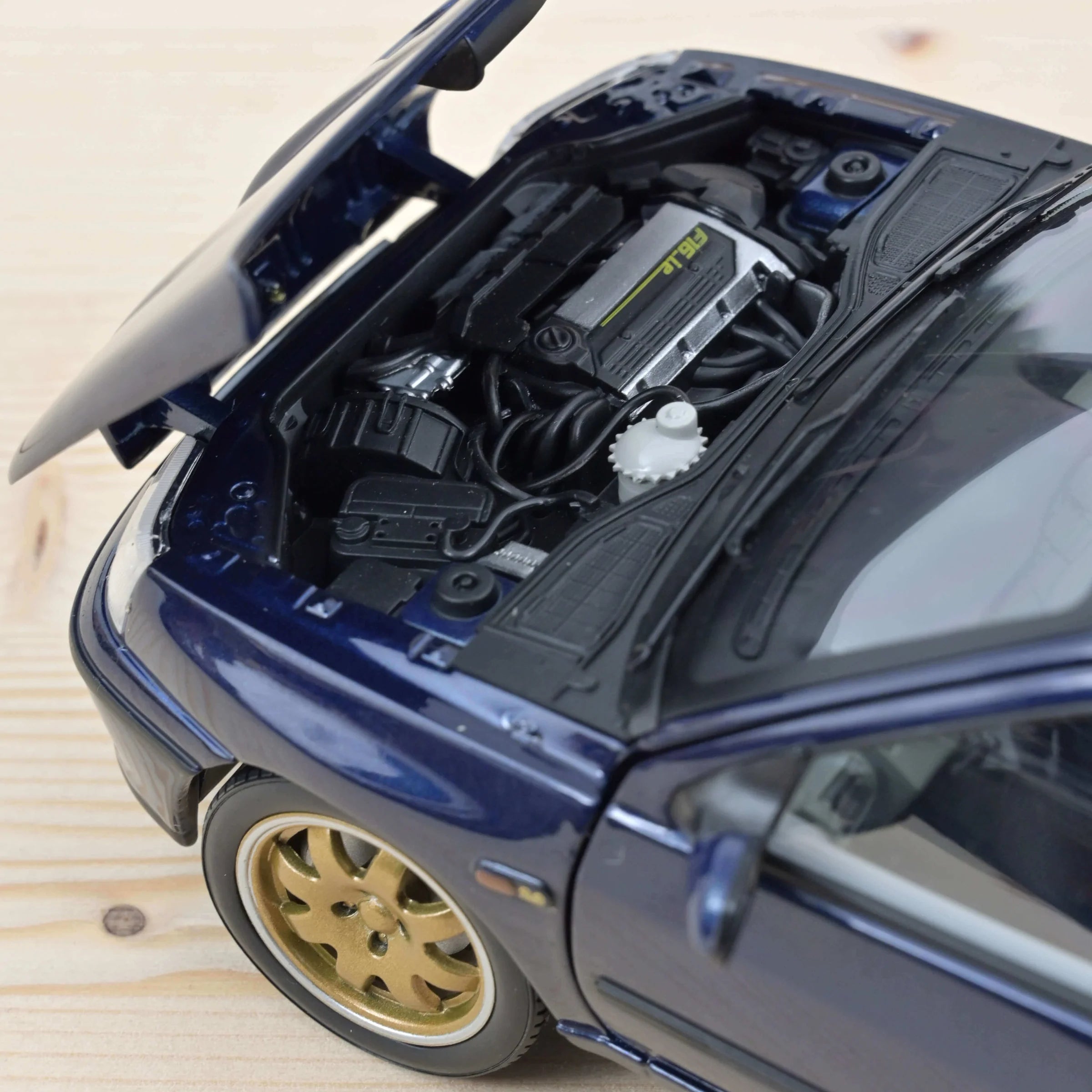 Model car with open hood showing engine components on a wooden surface