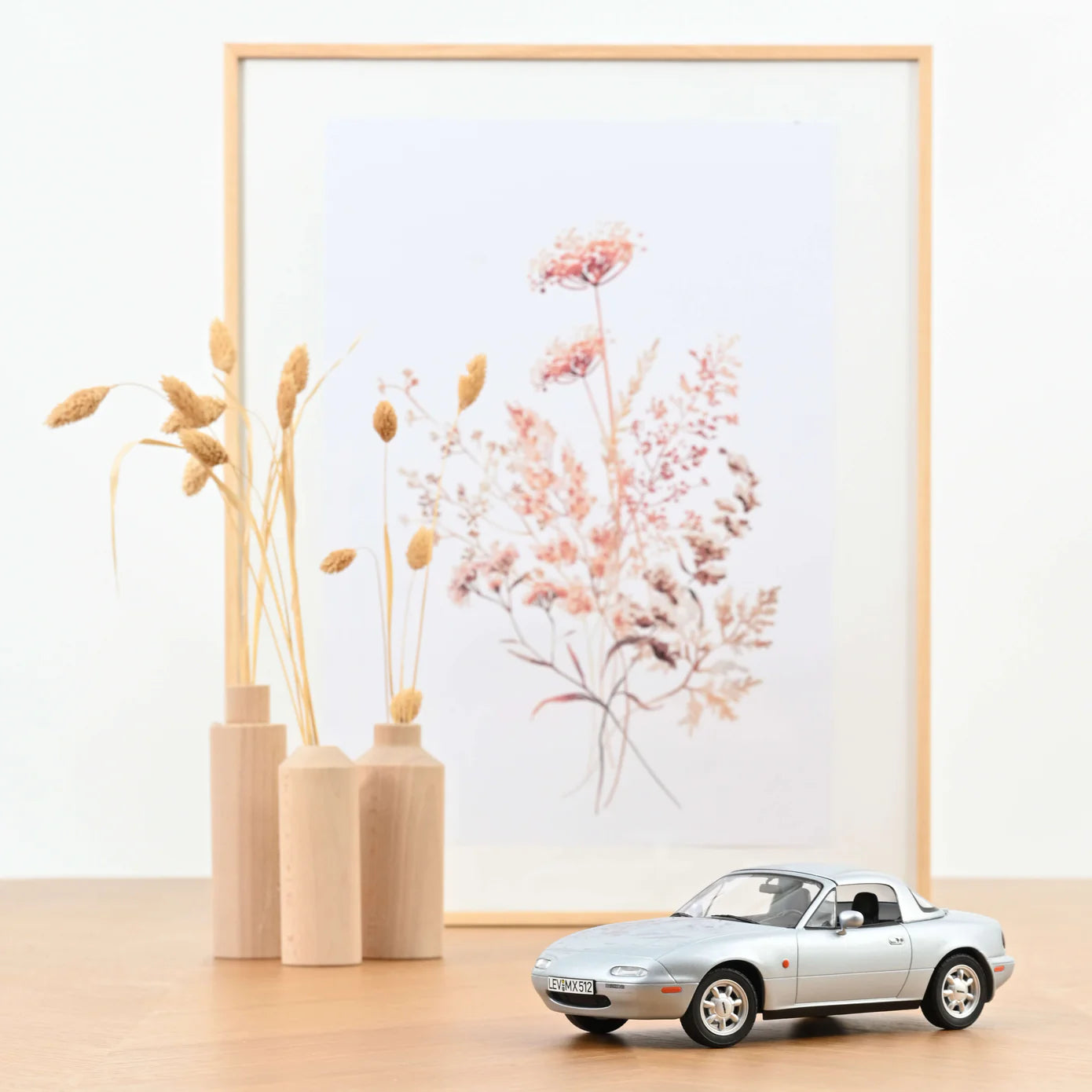 Framed floral art on a wall with decorative vases and a toy car below.