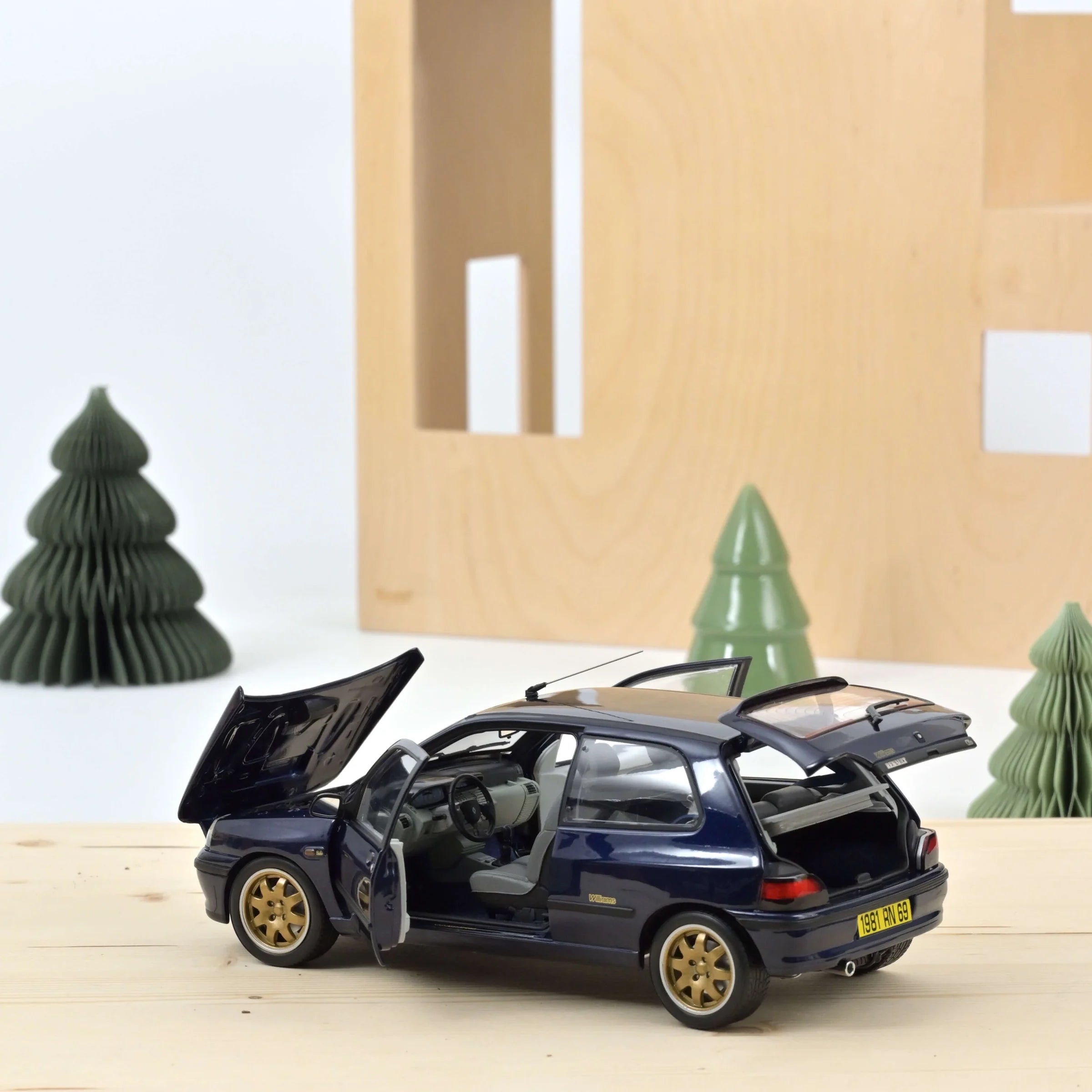 Model car with open doors on a wooden surface with decorative trees in the background
